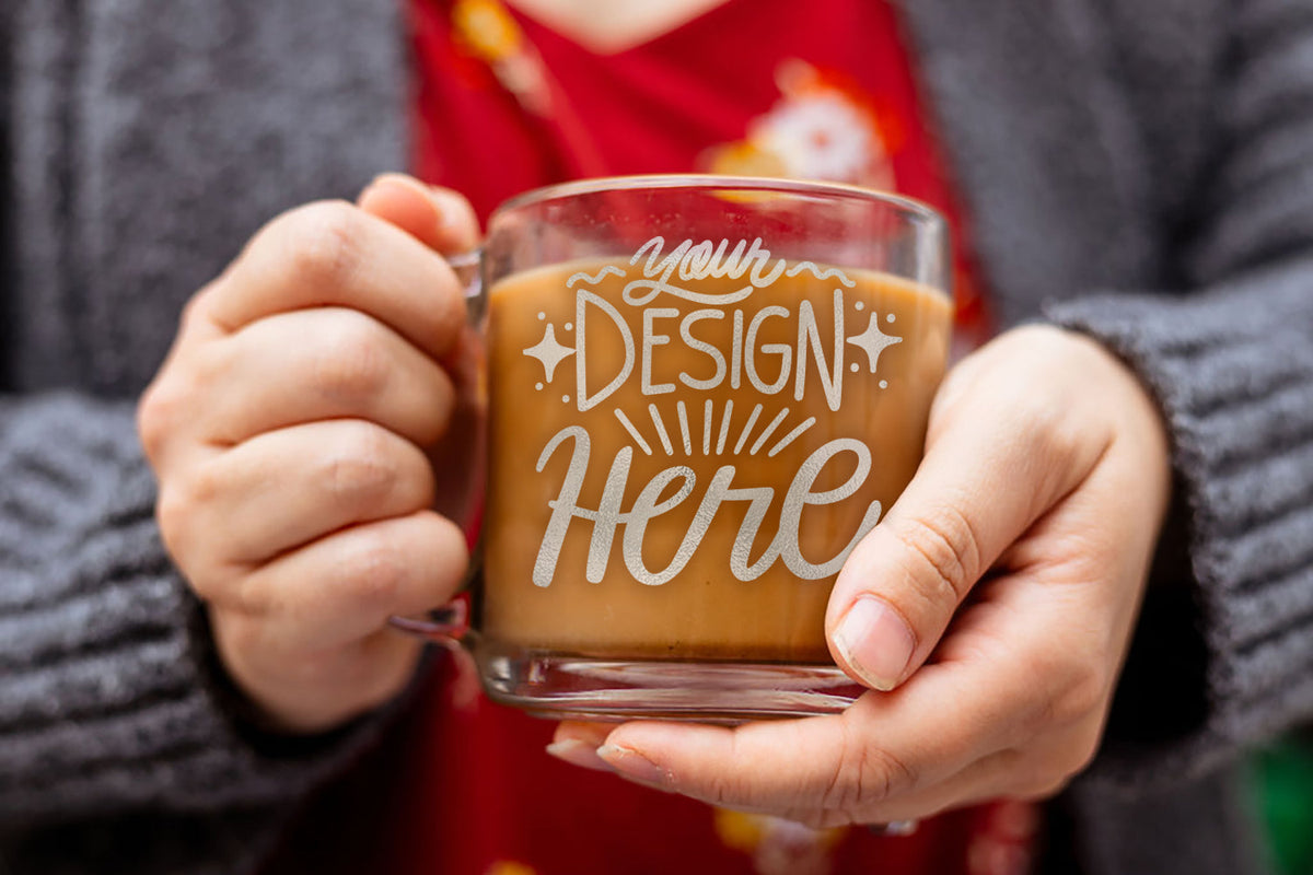 A zoomed in photo of two hands holding onto a mug filled with coffee and laser engraved with a text design of "Your Design Here"
