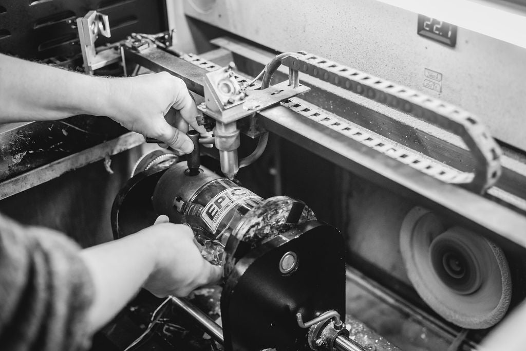 A black and white photo of two hands removing an engraved glass mug from a CO2 laser engraving machine.