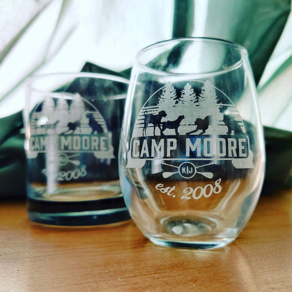 A stemless wine glass and whiskey glass that are both engraved with the Camp Moore logo