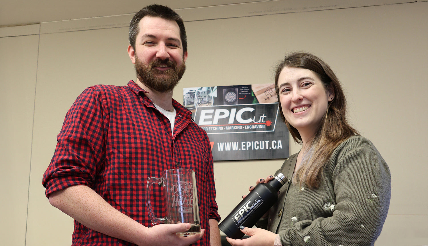 Jay and Sarah, the owners of EPICut, holding an engraved beer mug and water bottle in front of an 'EPICut' sign.