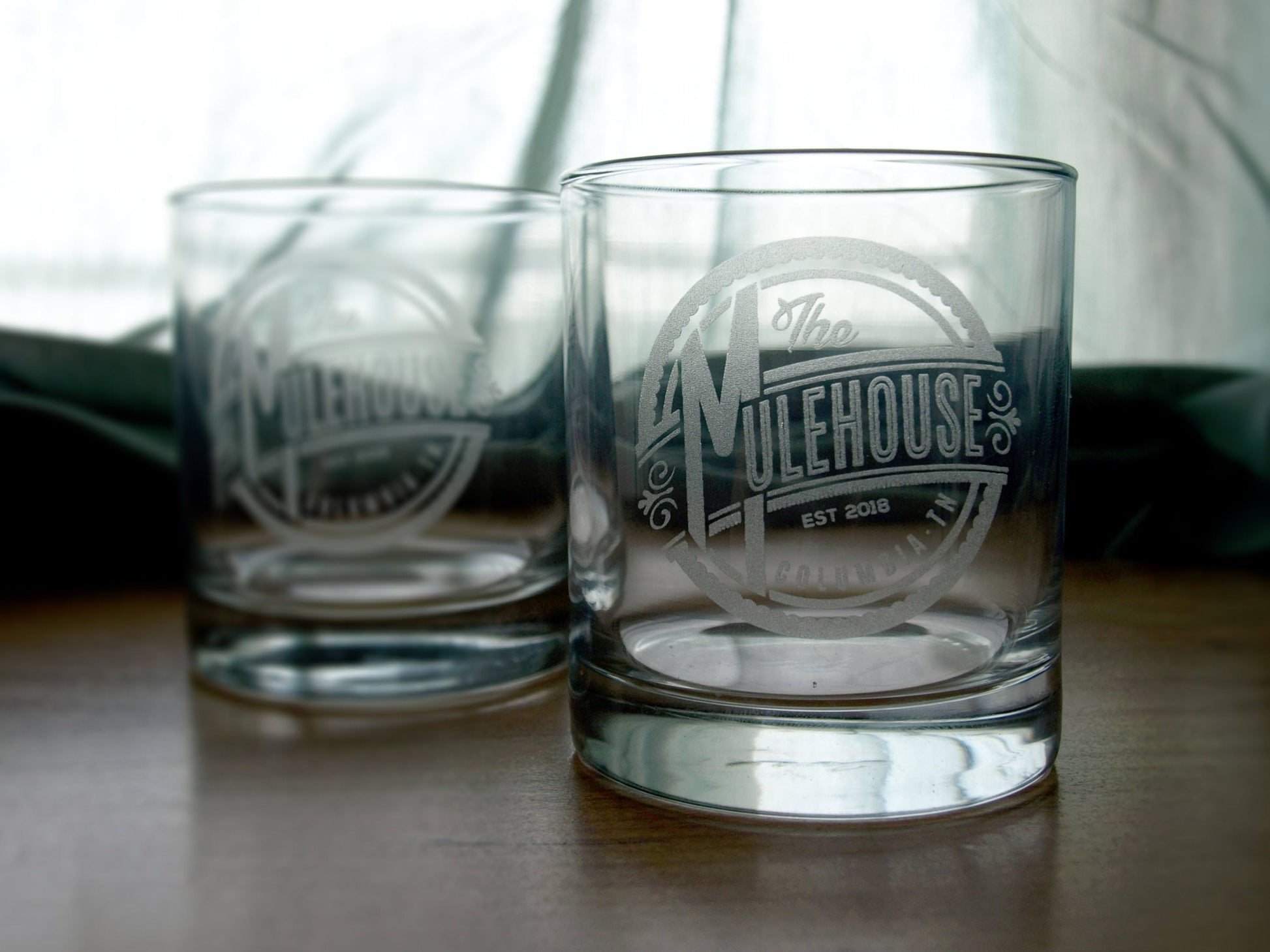 Two engraved whiskey glasses with The Mulehouse logo