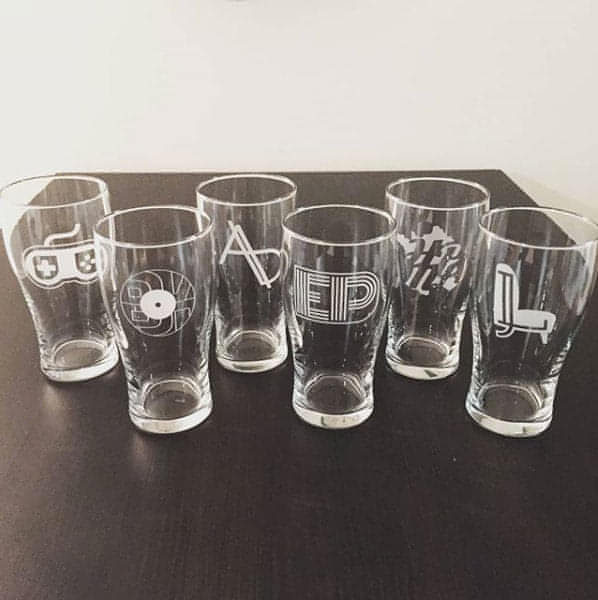 Several beer pint glasses engraved with a different logo monogram each